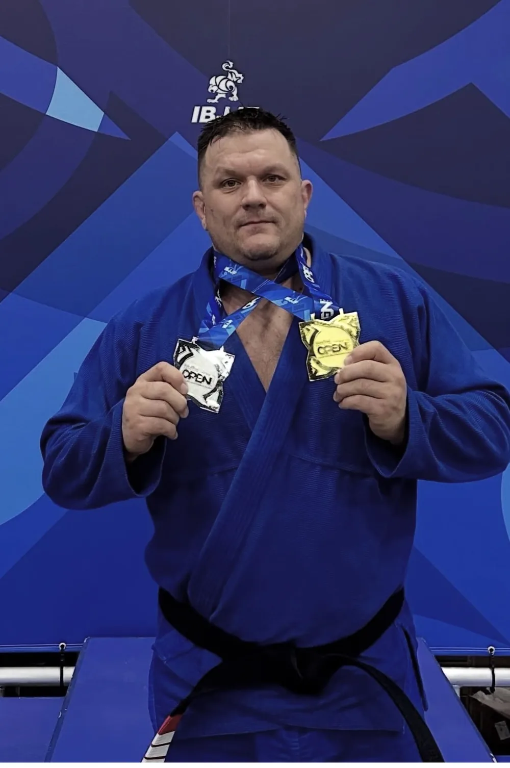 Coach Jorden Reichenbach in his black belt holding gold and silver IBJJF Open medals